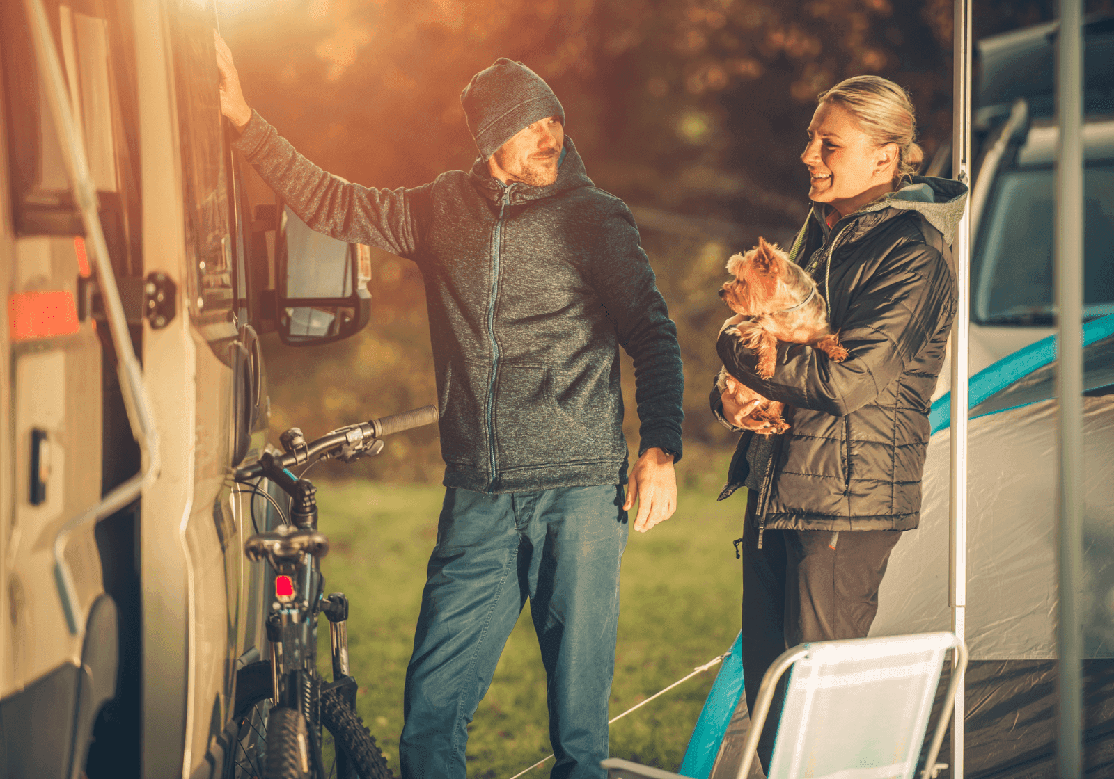 Ungt par med hund på campingplads foran deres autocamper.