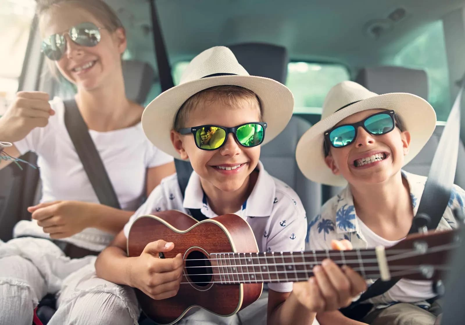 3 glade børn på bagsædet af en bil med solbriller og ukulele